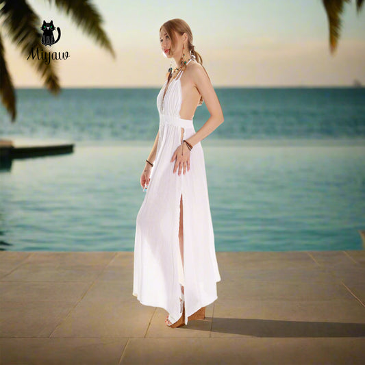 A stunning woman radiates elegance in a boho white cotton maxi dress, standing gracefully in front of a luxurious hotel.