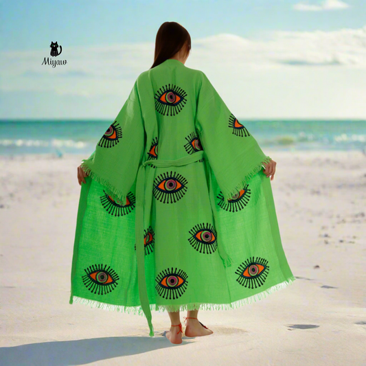 A woman wearing a handcrafted protective eye kimono stands on the beach.