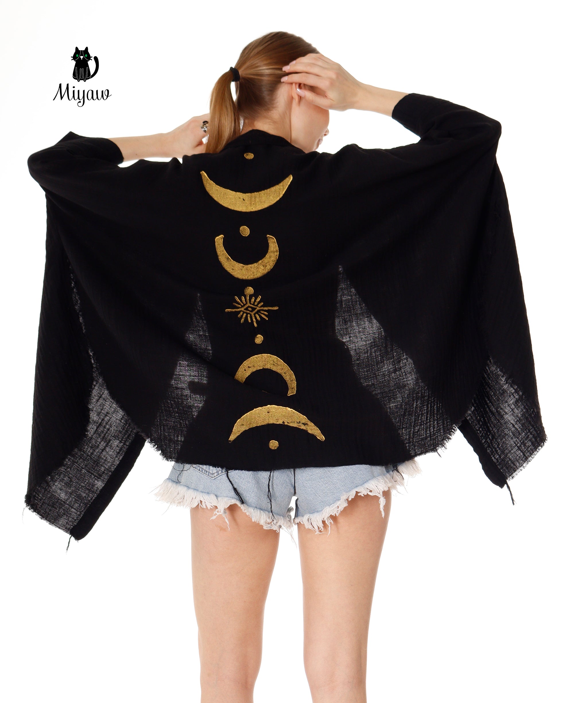 A woman wearing a black and gold boho style kimono with a sun and moon design, tied around the neck.