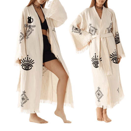 Woman wearing a cream-colored robe with black patterns in a bedroom setting, featuring the brand 'Miyaw'.