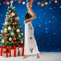 Woman in a black top and white pants with reindeer designs standing next to a decorated Christmas tree and presents.