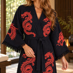 Close-up of the black robe showing red dragon prints, textured fabric, a tied black belt and fringe along the wide sleeves.