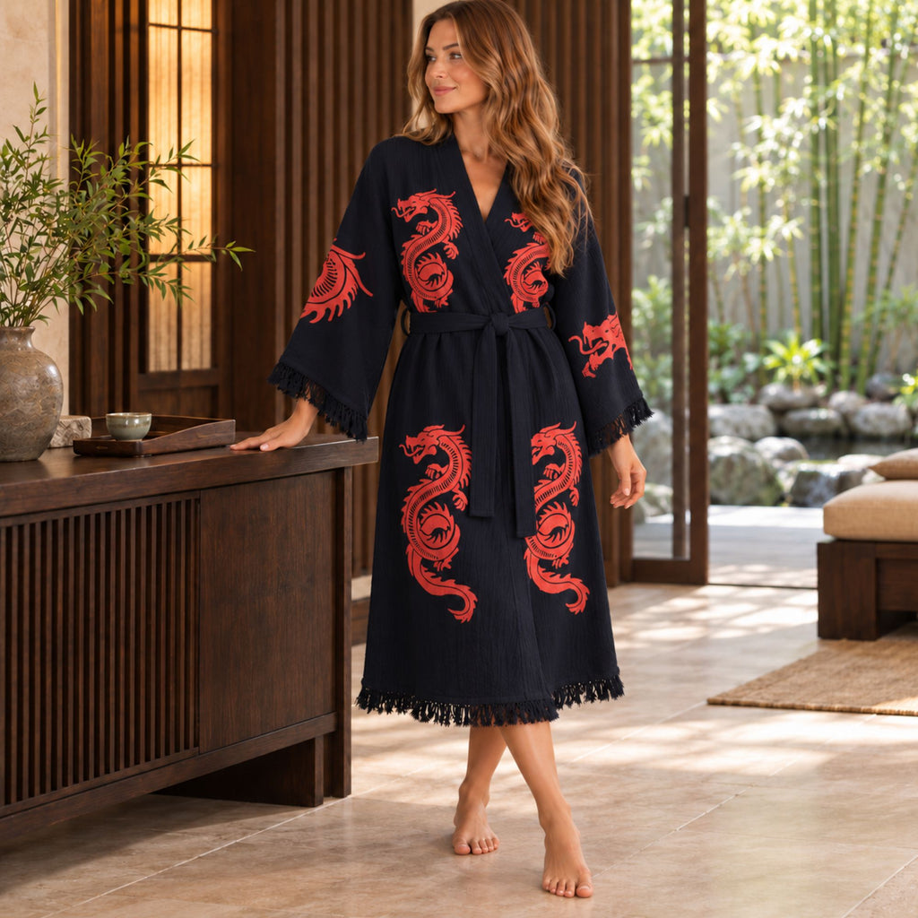 Woman standing beside a wooden console in a black kimono robe with red dragon prints, a tied waist belt and fringed cuffs and hem.