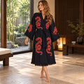 Woman wearing a black kimono robe with red dragon prints, wide fringed sleeves, a matching tie belt and a fringed hem.
